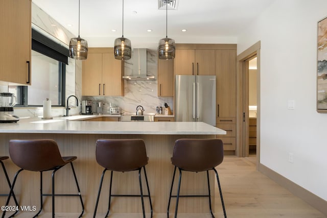 kitchen featuring decorative light fixtures, sink, stainless steel fridge, light brown cabinets, and wall chimney exhaust hood