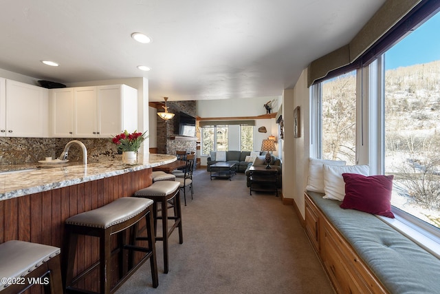 kitchen featuring a breakfast bar, tasteful backsplash, white cabinetry, carpet, and light stone countertops