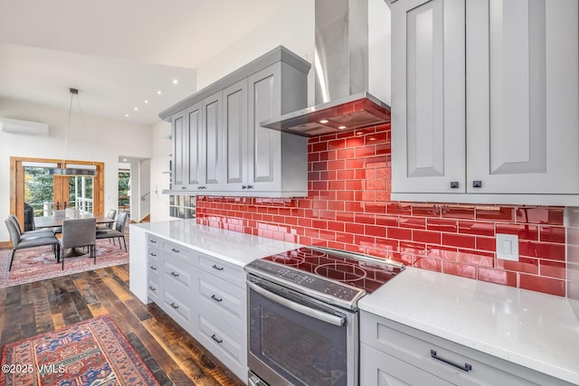 kitchen featuring stainless steel electric range oven, backsplash, a wall unit AC, decorative light fixtures, and wall chimney exhaust hood