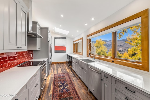 kitchen featuring tasteful backsplash, gray cabinetry, stainless steel appliances, and wall chimney exhaust hood