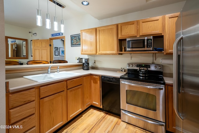 kitchen featuring sink, decorative light fixtures, light wood-type flooring, appliances with stainless steel finishes, and kitchen peninsula