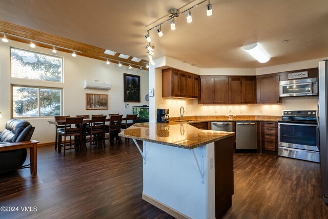 kitchen with an AC wall unit, sink, kitchen peninsula, stainless steel appliances, and dark wood-type flooring