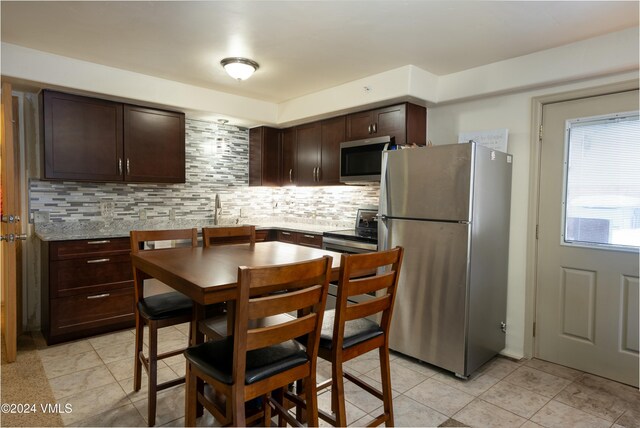 kitchen with tasteful backsplash, light stone counters, dark brown cabinets, light tile patterned floors, and stainless steel appliances