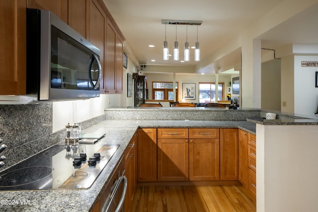 kitchen with stovetop, hanging light fixtures, kitchen peninsula, dark stone counters, and light hardwood / wood-style floors