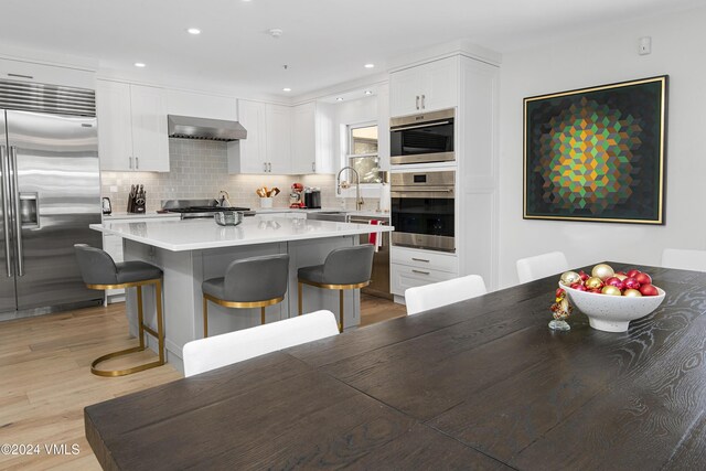 kitchen featuring a breakfast bar, white cabinets, a center island, stainless steel appliances, and wall chimney range hood