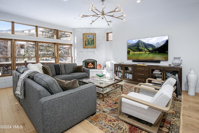 living room featuring a stone fireplace, light hardwood / wood-style flooring, and a notable chandelier