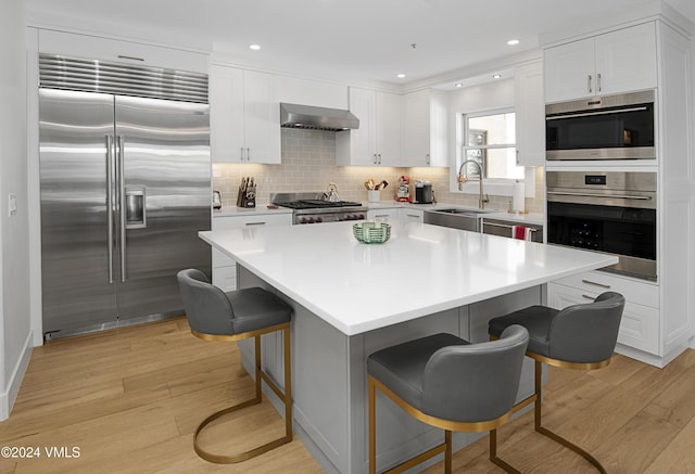 kitchen with a breakfast bar, sink, built in refrigerator, a center island, and wall chimney exhaust hood