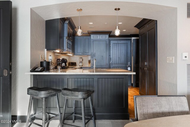 kitchen with sink, a breakfast bar, hanging light fixtures, blue cabinets, and kitchen peninsula