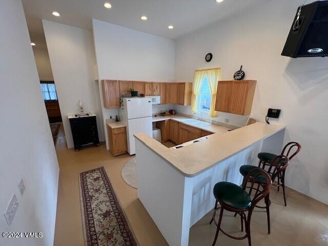 kitchen with plenty of natural light, kitchen peninsula, a high ceiling, and white fridge