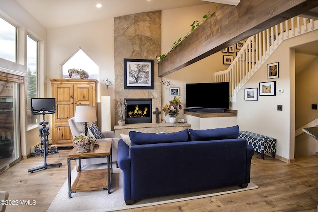 living room featuring baseboards, a tile fireplace, stairs, a towering ceiling, and light wood-type flooring