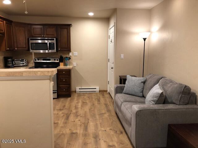 kitchen featuring light wood finished floors, light countertops, appliances with stainless steel finishes, tasteful backsplash, and baseboard heating