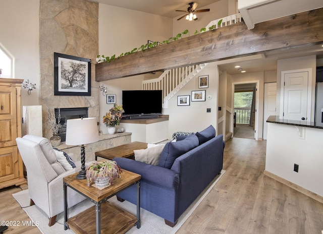 living area with a towering ceiling, stairway, light wood-style floors, ceiling fan, and a tile fireplace