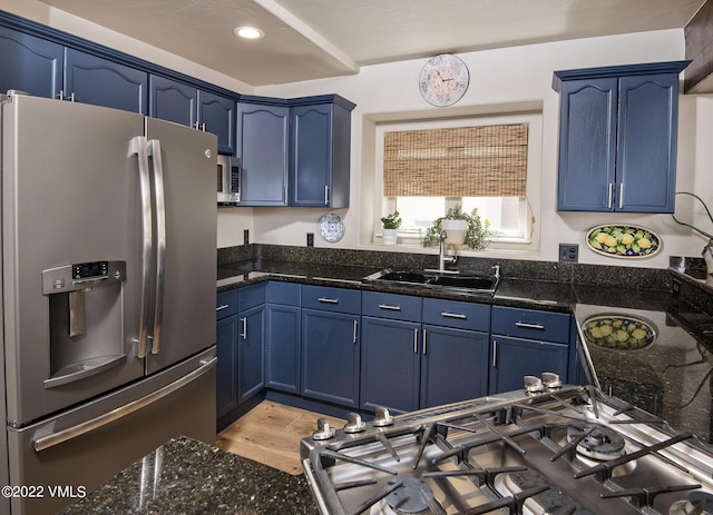 kitchen featuring dark stone counters, light wood-type flooring, appliances with stainless steel finishes, blue cabinets, and a sink