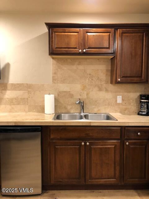 kitchen featuring dark brown cabinets, dishwasher, light countertops, and a sink