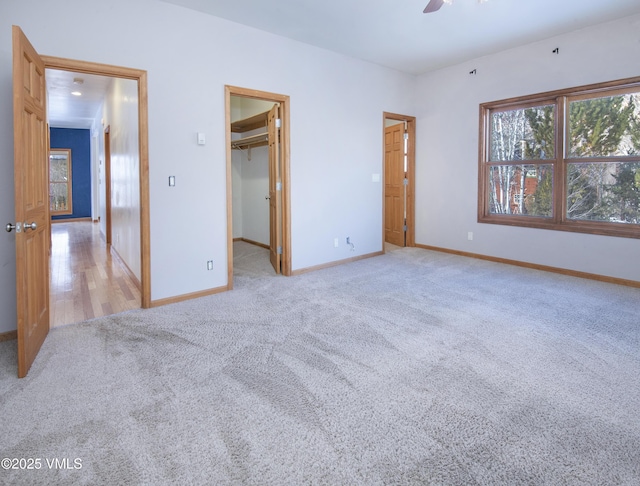 unfurnished bedroom featuring ceiling fan, a walk in closet, and light colored carpet