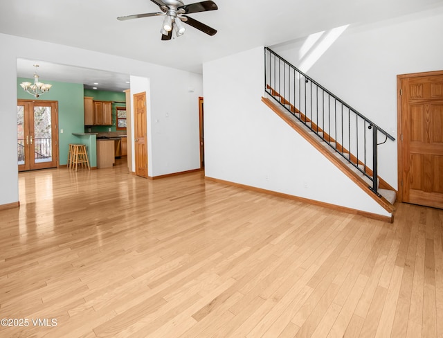 unfurnished living room with ceiling fan with notable chandelier, light hardwood / wood-style flooring, and french doors