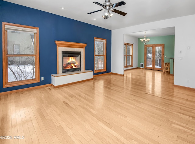 unfurnished living room featuring ceiling fan with notable chandelier, light wood-type flooring, and french doors