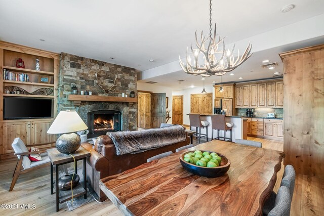 dining area with built in shelves, a fireplace, a chandelier, and light wood-type flooring