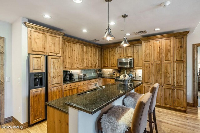 kitchen with pendant lighting, sink, dark stone countertops, paneled built in fridge, and a center island with sink