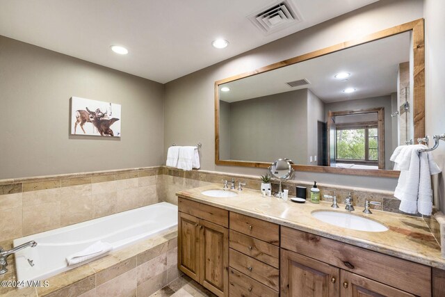 bathroom featuring a relaxing tiled tub and vanity