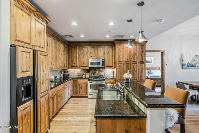 kitchen featuring sink, hanging light fixtures, appliances with stainless steel finishes, a kitchen breakfast bar, and a kitchen island with sink