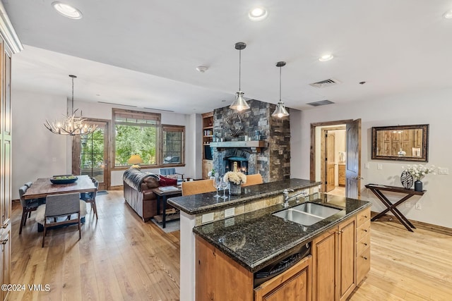 kitchen with a stone fireplace, sink, decorative light fixtures, light hardwood / wood-style flooring, and dark stone countertops