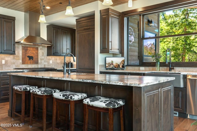 620 Jouflas Ranch Rd, Wolcott, CO 81655 - kitchen with wall chimney range hood, dark brown cabinets, an island with sink, dark wood-style flooring, and decorative backsplash