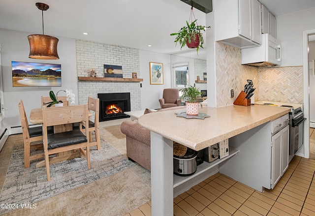 kitchen featuring range with electric stovetop, tasteful backsplash, white cabinetry, hanging light fixtures, and a brick fireplace