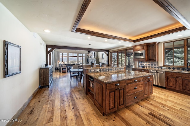 kitchen featuring appliances with stainless steel finishes, a raised ceiling, decorative light fixtures, and a kitchen island