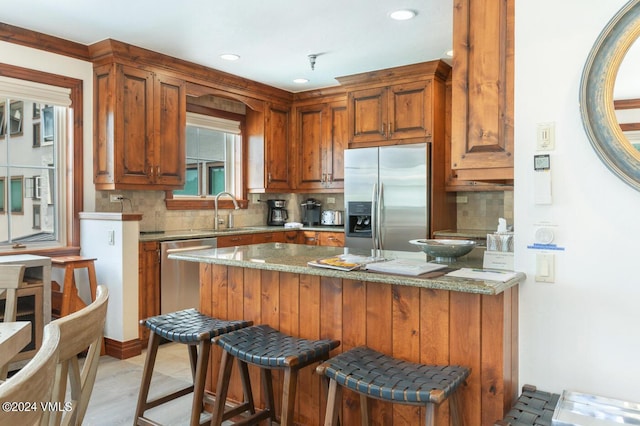 kitchen with a breakfast bar, sink, appliances with stainless steel finishes, light stone countertops, and decorative backsplash