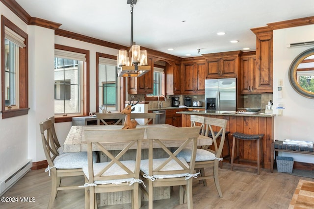 kitchen with decorative light fixtures, baseboard heating, stainless steel appliances, light hardwood / wood-style floors, and backsplash