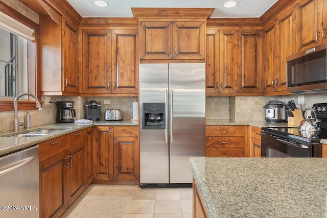 kitchen featuring stainless steel appliances, sink, backsplash, and light stone counters