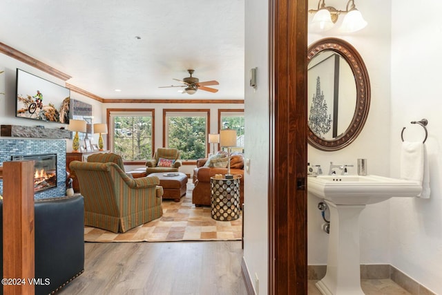 living room featuring sink, light hardwood / wood-style flooring, ceiling fan, a fireplace, and ornamental molding