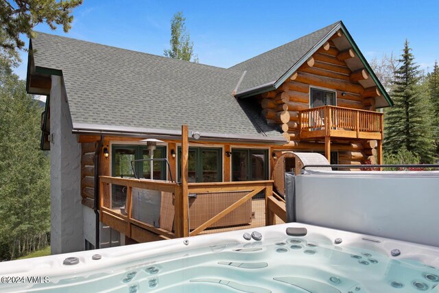 rear view of house featuring a wooden deck and a hot tub