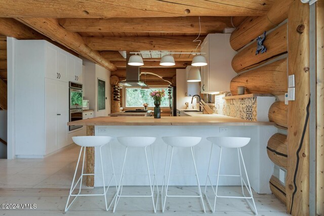 kitchen featuring double oven, decorative light fixtures, sink, white cabinets, and kitchen peninsula