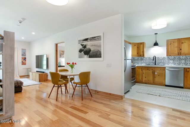 kitchen with appliances with stainless steel finishes, decorative backsplash, light wood-type flooring, and decorative light fixtures