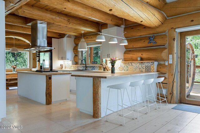 kitchen featuring a kitchen island, decorative light fixtures, rustic walls, white cabinets, and island exhaust hood