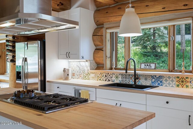 kitchen featuring island range hood, butcher block countertops, decorative light fixtures, white cabinets, and stainless steel appliances