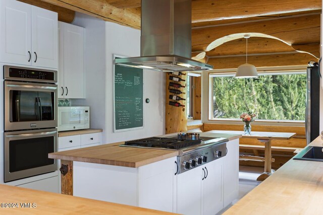 kitchen with butcher block counters, island range hood, appliances with stainless steel finishes, pendant lighting, and white cabinets