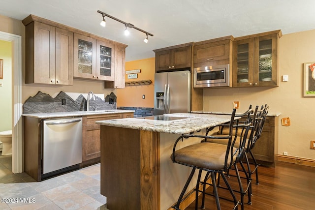 kitchen with sink, appliances with stainless steel finishes, a kitchen breakfast bar, light stone counters, and light wood-type flooring