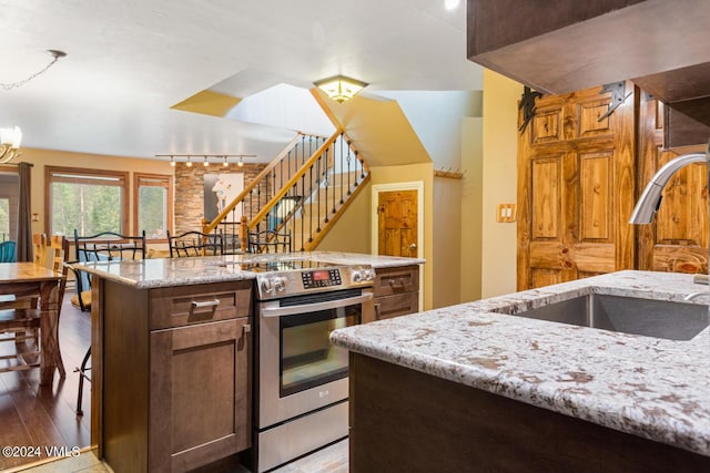 kitchen featuring sink, hardwood / wood-style flooring, electric range, light stone countertops, and a center island with sink