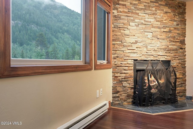 interior details with a stone fireplace, baseboard heating, and hardwood / wood-style flooring