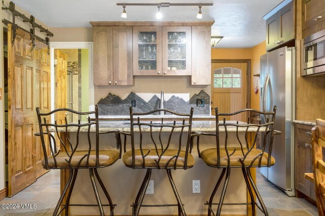 interior space with appliances with stainless steel finishes, a barn door, light stone countertops, and a kitchen bar