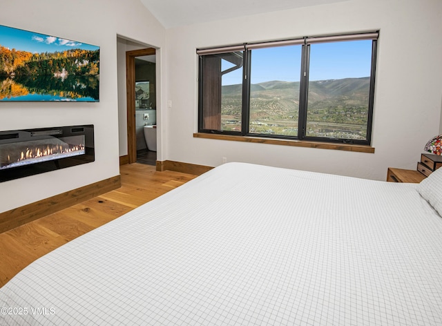 654 Gold Dust Dr W, Edwards, CO 81632 - bedroom with wood finished floors, a glass covered fireplace, vaulted ceiling, and baseboards