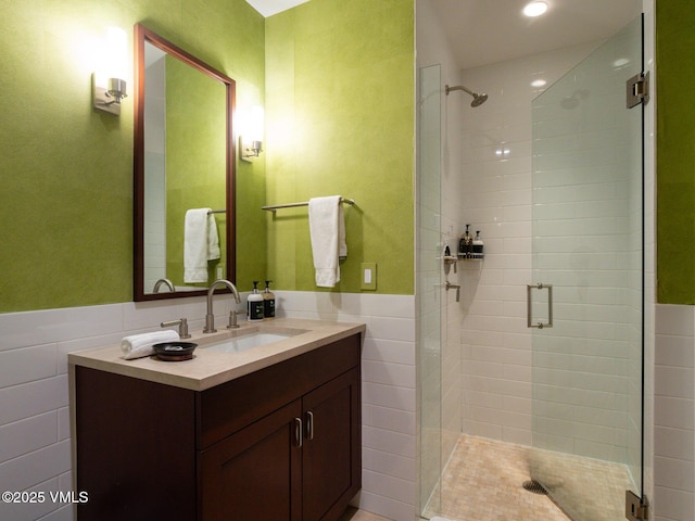 bathroom with a wainscoted wall, a stall shower, tile walls, and vanity