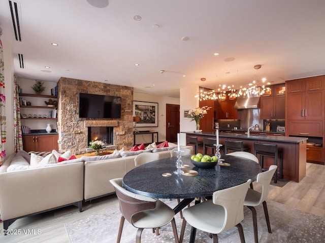 dining area featuring recessed lighting, a stone fireplace, a chandelier, and light wood finished floors