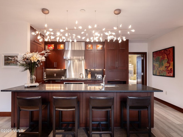 bar featuring wood finished floors, stovetop, a sink, wall chimney exhaust hood, and backsplash