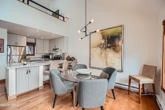 dining space featuring light hardwood / wood-style flooring, sink, a chandelier, baseboard heating, and a high ceiling