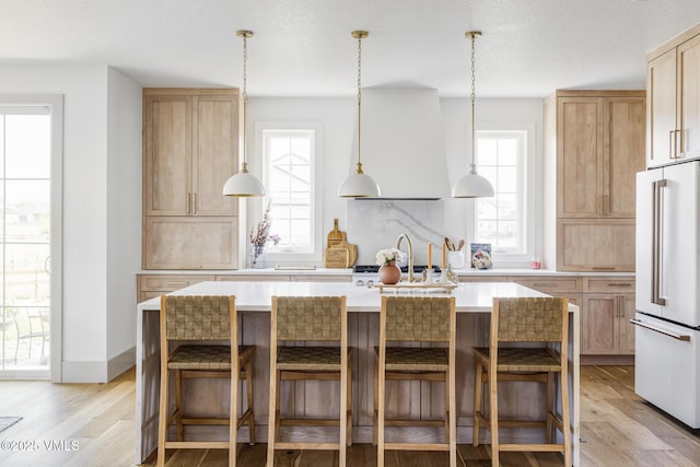 kitchen with an island with sink, high end fridge, and exhaust hood