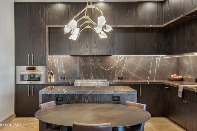 kitchen with dark brown cabinetry, hanging light fixtures, backsplash, and oven